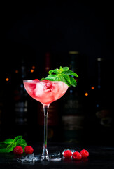 Raspberry cocktail with white rum, sugar syrup, fruit juice, lime, berry and ice in glass. Black bar counter background