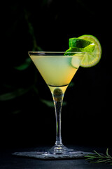 Classic alcoholic cocktail with vodka, syrup, lime, juice and ice in martini glass, dark background