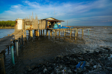 A peaceful sunset view of a wooden house stretching into the sea, with waves gently lapping the sandy shore