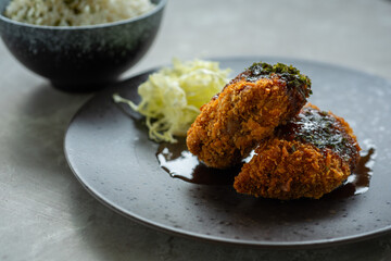 Japanese food menchi katsu メンチカツ and rice, served with black plate and white bowl, over stone tile table, cafe environmen