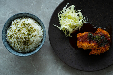 Japanese food menchi katsu メンチカツ and rice, served with black plate and white bowl, over stone tile table, cafe environmen
