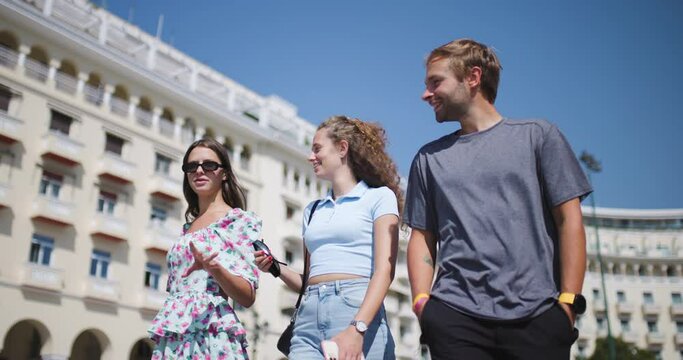 Tourists walking talking and smiling. Man with two women friends moving around the city.