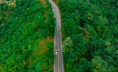 Aerial view of dark green forest road and white electric car Natural landscape and elevated roads Adventure travel and transportation and environmental protection concept