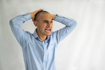 Confused shaved young man with one eyebrow raised and with his hands on his head