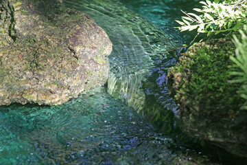 Close-up on clear turquoise water flowing between mossy boulders in a stream