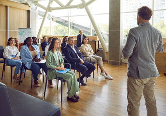 Group of people having a business training with a professional coach. Company staff meeting with a team mentor. Diverse audience sitting on chairs in the office listening to a man giving a speech