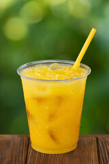 disposable plastic glass of cold orange juice with ice and straw