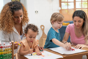 Happy family. Mother and kids together paint. Woman helps the child. Little children with kindergarten teacher drawing at table indoors. Learning and playing	
