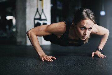 Fototapeta premium Push ups, woman and training in gym on floor for workout, health and wellness with power or resilience. Strong, athlete and exercise in sports club for fitness, competition and body goals with muscle