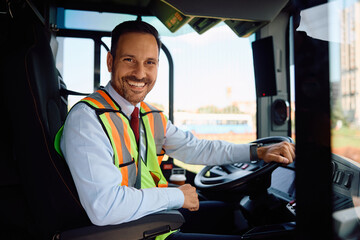 Happy public transport driver behind the wheel in bus cabin looking at camera.