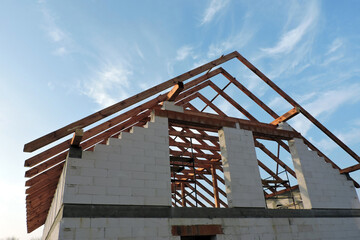 An "A" frame timber roof truss in a house under construction seen from the bottom, walls made of aac blocks, a rough window opening, a reinforced brick lintel, a scaffolding