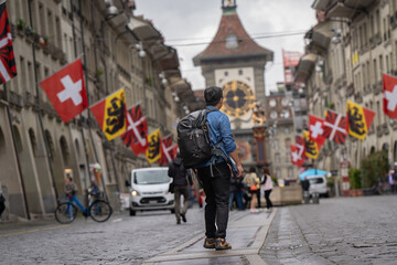 tourist go to travel walk in walking street see old building architecture nation flag and clock tower in Bern Switzerland spring season