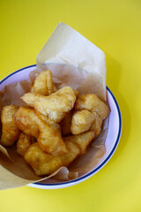 Deep-fried dough sticks or Patongko on yellow background. Concept of breakfast, deep frying, crispy texture, and Asia culture. Patongko is famous Thai street food. Deep-fried dough sticks in pink bowl