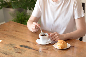 Woman in a white T-shirt with a cup of coffee and a croissant at a table in a café