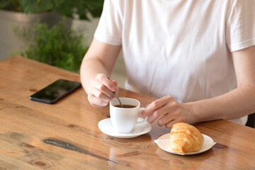 Woman in a white T-shirt with a cup of coffee and a croissant at a table in a café