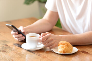 Woman in a white T-shirt with a cup of coffee and a croissant at a table in a café