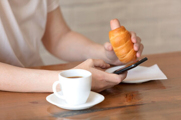 Woman in a white T-shirt with a cup of coffee and a sausage at a table in a café