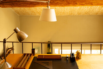 Workplace with desk and work lamps on the mezzanine floor. Wooden beams under the roof