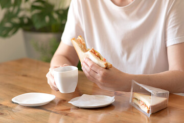 Woman in a white T-shirt with a cup of coffee and a sandwich at a table in a café