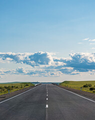 Endless country road stretching into horizon under bright blue sky and fluffy clouds in daytime