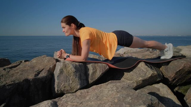 Young pretty woman doing plank exercise for her training by the sea at the morning
