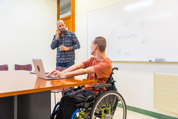 Man with disability and colleague working with laptop in coworking
