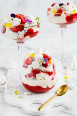 Eton mess - traditional english dessert with meringues, whipped cream and fresh strawberries  in a glasses on a light background. Selective focus