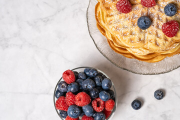 Top view of Belgian waffle and mix of raspberries and blueberries on marble background. Delicious...
