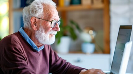 Fototapeta premium senior man using laptop computer, smiling and focused on online activity at home.
