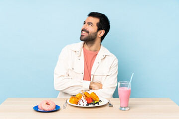 Man at a table having breakfast waffles and a milkshake looking up while smiling