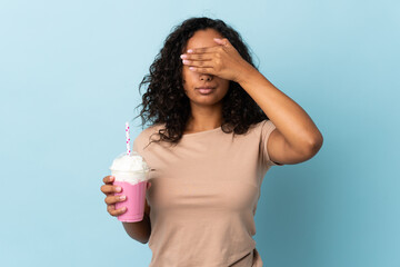 Teenager girl  with strawberry milkshake isolated on blue background covering eyes by hands. Do not want to see something