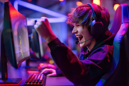 Young gamer enthusiastically celebrating a victory while playing computer games, surrounded by colorful neon lights in a gaming club. Esports