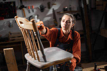 Young woman painting old wooden chair in grey color with paint brush working in her workshop. Restoration of the chair. Painting furniture. renovation, diy and furniture restoration