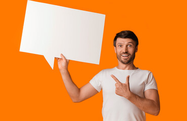 A man holds a blank speech bubble and points to it with a wide smile, standing against a bright orange background.