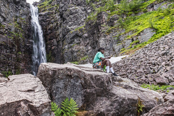 Woman sits and takes a rest with her mobile phone at Sweden's highest waterfall Njupeskär.