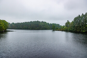 Lake Robertville next to dam wall surrounded by green leafy pine trees against cloud covered sky,...