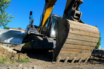 Fototapeta premium Idle excavator bucket digger construction site town street renovation clear sky wide angle