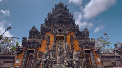 Intricate Balinese temple with detailed carvings and statues against a blue sky. Traditional architecture showcases cultural and artistic heritage in a serene setting.