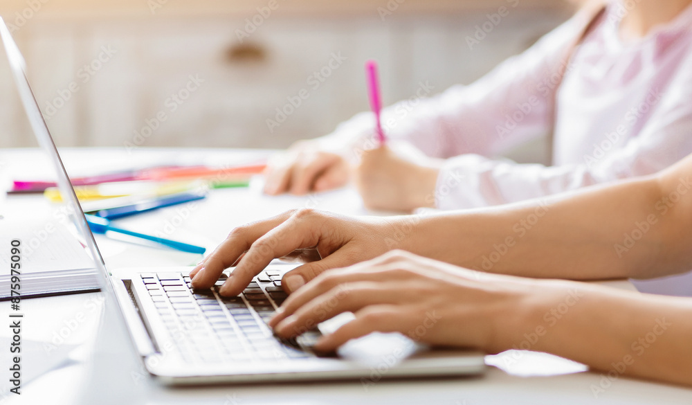 Poster woman is typing on a laptop computer while sitting at a desk. there are colored pencils and a notebo