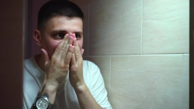 A man of European appearance moisturizes his face with cream.
A man in front of a mirror applies cream to his face.
Man treating skin disease on face
