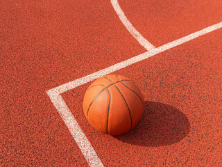 Above view sports background of orange basketball ball lying on court floor lit by sunlight, copy space