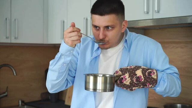A man is preparing soup.
Hot soup in a saucepan.
A man tests his food for salt.
A man holds a saucepan with an oven mitt.
Hot dishes, fire, gas, stove