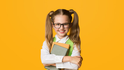 School Kid. Smiling Elementary Student Girl Hugging Books Happy About Back-To-School Standing On Yellow Studio Background