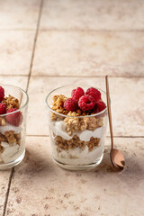 Berry dessert in glass with granola, fresh raspberries, yogurt or cream cheese. Healthy breakfasr concept, on beige tile background with text space