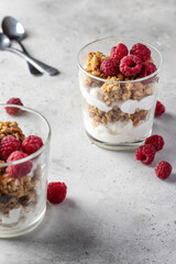 Berry dessert in glass with granola, fresh raspberries, yogurt or cream cheese. Healthy breakfasr concept, vegetarian on gray background