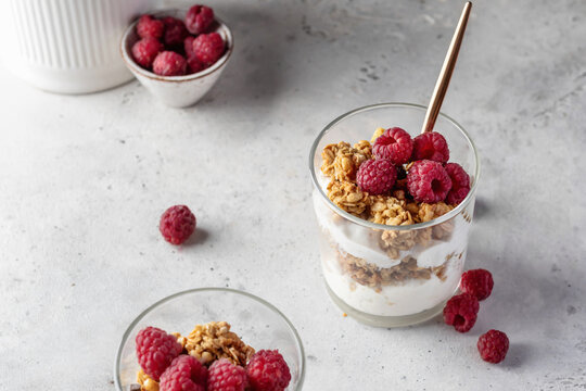 Berry dessert in glass with granola, fresh raspberries, yogurt or cream cheese. Healthy breakfasr concept, vegetarian on gray background