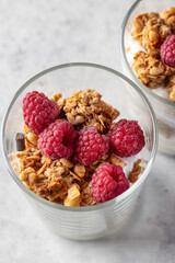 Berry dessert in glass with granola, fresh raspberries, yogurt or cream cheese. Healthy breakfasr concept, vegetarian on gray background close up