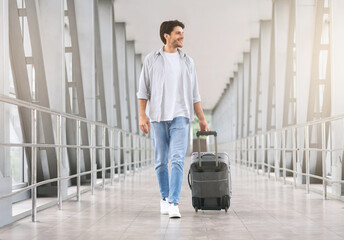 Young man walking in airport walkway with luggage, free space