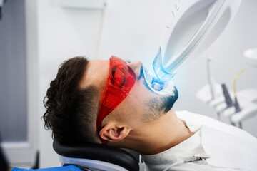 Patient whitens his teeth while treatment in dental cabinet. Ultraviolet teeth whitening procedure...