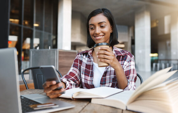 Girl, phone and coffee at university, outdoor or smile for meme, mobile app and notes for development. Person, laptop and reading on break, social media and tea with learning for education at college